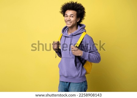 Attractive smart smiling university student with backpack looking at camera isolated on yellow background, copy space. Education concept