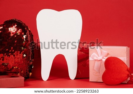 Valentine's Day in dentistry - a large white tooth, a heart and boxes of gifts on a red background, a place for text.