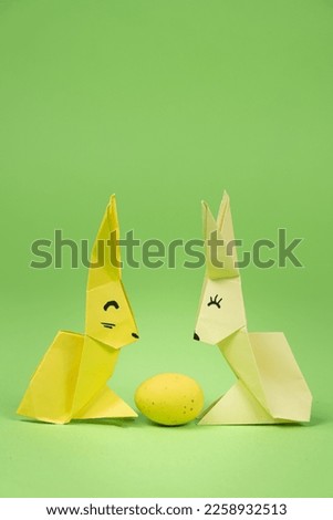 Easter origami - two paper bunnies and an egg, green background. Crafts for the holiday, do it yourself