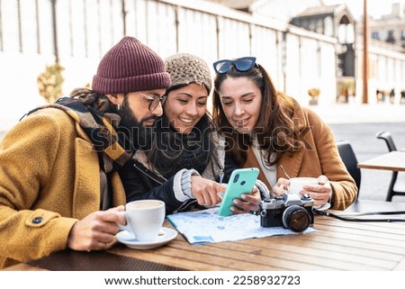 Young friends looking at cell phone sitting in cafe, checking tourist city map during winter vacations 