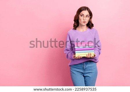 Photo of unsure dreamy girl dressed purple pullover eyewear looking empty space holding book pile isolated pink color background