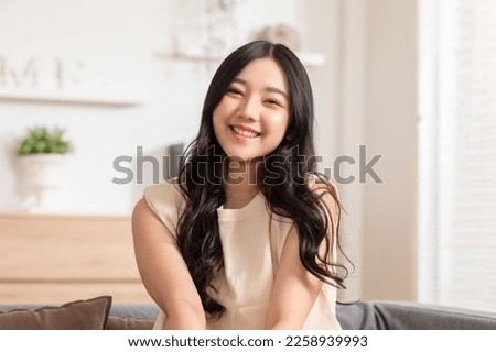 Stunning Beautiful Attractive Asian young woman sit on couch or sofa looking at camera and smile happiness and comfortable at home.Cute girl smile cross arm confident and relax in living room Royalty-Free Stock Photo #2258939993