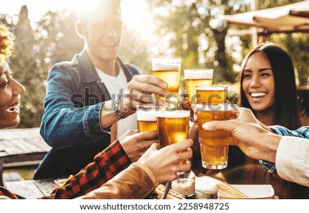 Happy friends cheering beer glasses at brewery pub garden - Group of young people enjoying happy hour sitting at bar table - Life style concept with guys and girls having dinner party together Royalty-Free Stock Photo #2258948725