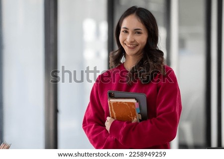 Image of young indian girl asian woman, company worker in dress red shirt, smiling and holding digital tablet, standing over office background