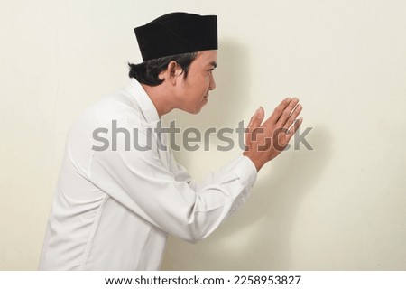 asian man with greeting gesture apologizing. hand gesture greeting symbol of welcome, apologize, greeting. Indonesian man wearing white shirt and cap on isolated white background