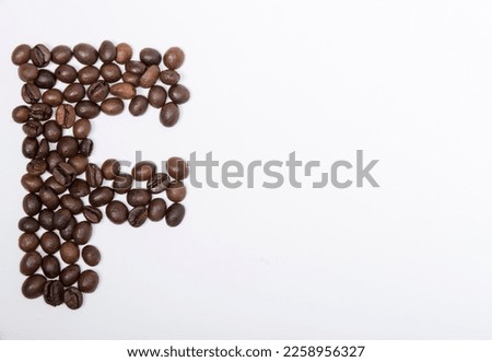 F is a capital letter of the English alphabet made up of natural roasted coffee beans that lie on a white background. Plenty of space to put text or pictures, top view and studio photography.