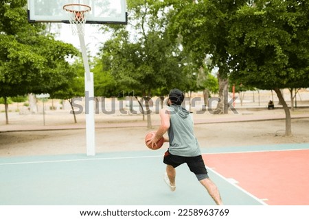 Rear view of a young man ready to jump and throw the ball in the hoop while playing basketball