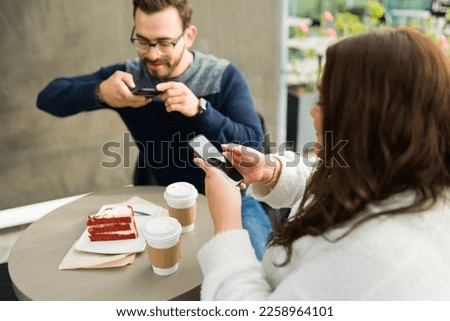 Influencer attractive couple eating at a restaurant cafe and taking pictures with smartphones to the coffee and cake to post it on social media 