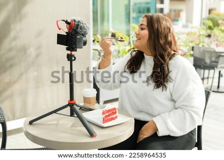 Chubby latin influencer woman doing a restaurant or cafe review for social media while filming video content with a camera