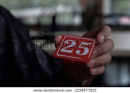 Hand holding plat Number 25 with red background