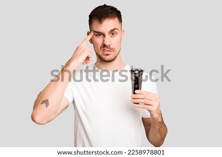 Young man holding a shaving machine cut out isolated showing a disappointment gesture with forefinger.
