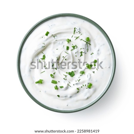 Green bowl of sour cream dip sauce with herbs isolated on white background, top view
