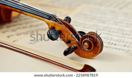 An old antique violin and a bow on a table with yellowed sheet music close-up. Royalty-Free Stock Photo #2258987819