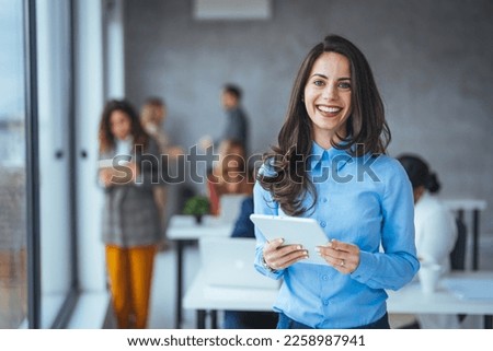 Young businesswoman standing in office with a digital tablet. Confident businesswoman in office. Beautiful businesswoman standing and working on a digital tablet computer in the modern office Royalty-Free Stock Photo #2258987941