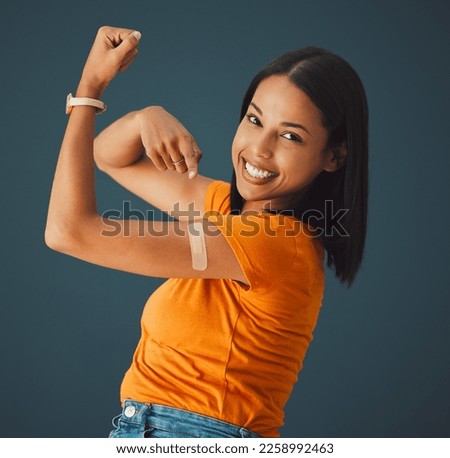 Vaccine, plaster and portrait of a woman in a studio with a strength gesture after being vaccinated. Happy, smile and proud female model with a vaccination band aid isolated by a dark blue background