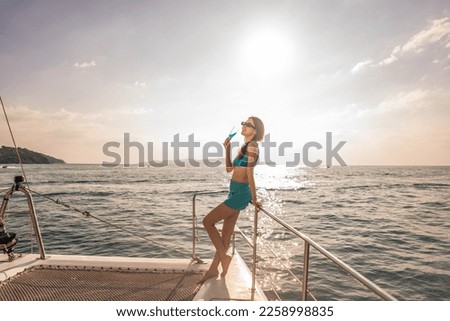 Asian woman in bikini drinking champagne while having party in yacht. Attractive beautiful female tourist hanging out celebrate holiday vacation trip while catamaran boat sailing during summer sunset.