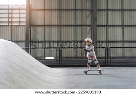 asian child skater or kid girl playing skateboard or ride surf skate up to wave ramp or wave bank to fun bottom turn in skate park by extreme sports surfing to wear helmet knee support for body safety Royalty-Free Stock Photo #2259001193