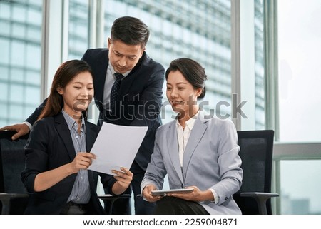 team of three asian businesspeople sitting standing by window discussing business in office Royalty-Free Stock Photo #2259004871
