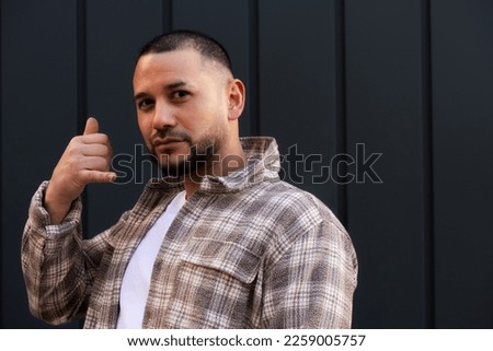 Handsome young man with beard making telephone gestures with hand and fingers as if talking on the phone. Communicating concepts.