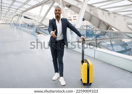 Smiling young black businessman extending hand for handshake at camera while standing in modern airport terminal, african american male entrepreneur in suit greeting somebody, copy space Royalty-Free Stock Photo #2259009323