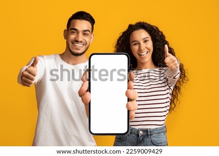 Mobile Mockup. Happy Arabic Couple Holding Blank Smartphone And Showing Thumbs Up At Camera, Smiling Middle Eastern Man And Woman Recommending New App Or Website, Posing On Yellow Background, Collage Royalty-Free Stock Photo #2259009429