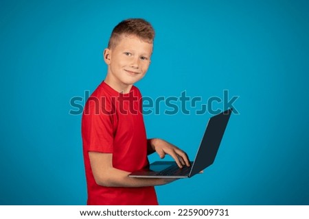 Smiling Preteen Boy Using Laptop Computer While Standing Over Blue Studio Background, Happy Caucasian Male Child Typing On Keyboard, Study Online Or Playing Video Games In Internet, Copy Space