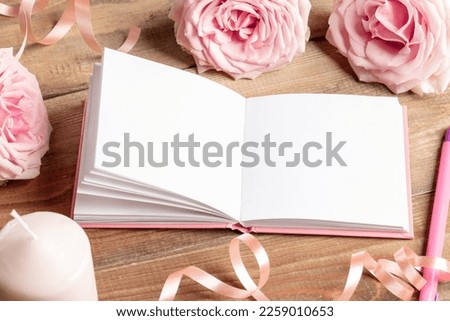 Opened white empty blank notepad, gentle, pink roses, candle, pen, ribbon on old wooden table.