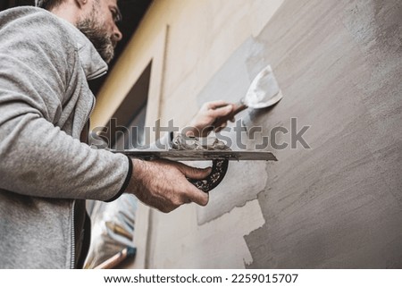 Renovation of the building facade - construction industry. Worker man (plasterer) plastering exterior walls of a house. Royalty-Free Stock Photo #2259015707