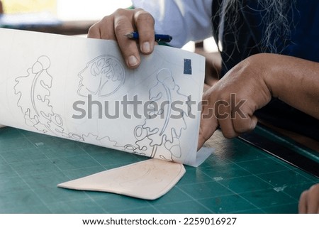 Close-up hand-raising tracing paper which is clear paper, with clear pattern on paper, compared to get same shape size as cut snake skin, press to get pattern on snake skin before trimming. Royalty-Free Stock Photo #2259016927