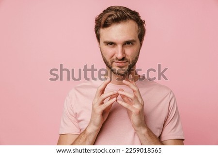 Tricky young bearded man wearing pink t-shirt clasping hands isolated over pink studio wall Royalty-Free Stock Photo #2259018565