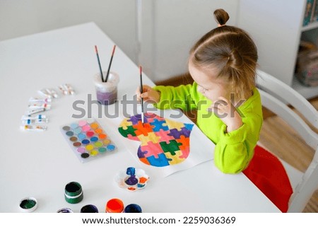A three-year-old girl draws a drawing for children suffering from autism with a picture of a heart from puzzles. Learn to be tolerant from childhood
