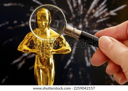 Golden Oscar award statue  under magnifying glass on fireworks background, closeup