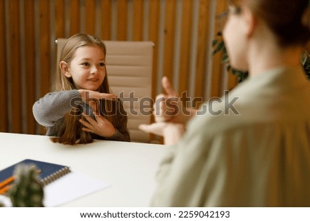 Sign language, smiling deaf-mute little girl communicates with her mother at the table.