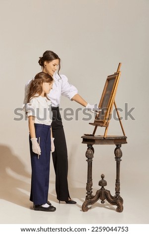 Hobby. Portrait of young woman and little girl, mother and daughter painting picture isolated over light background. Concept of retro style, fashion, elegance, 60s, 70s, family. Copy space for ad