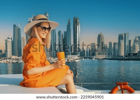 smiling woman in orange dress with drink on luxury yacht in Dubai at sunset. city skyline in background. copy space