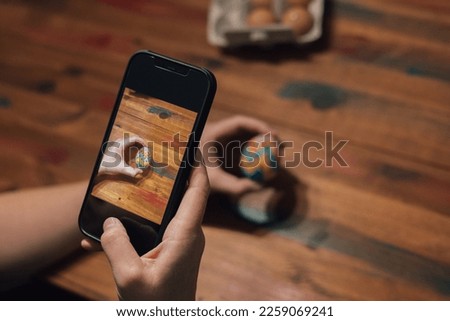 Hand taking a picture of a freshly painted easter egg with a mobile phone