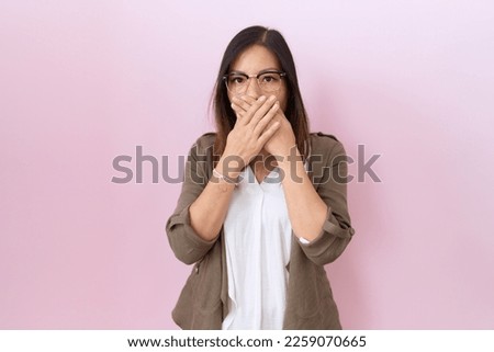 Middle age chinese woman wearing glasses over pink background shocked covering mouth with hands for mistake. secret concept. 