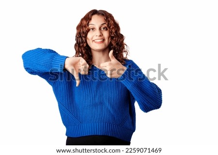 Cheerful woman wearing blue pullover sweater isolated over white background making thumbs up and thumbs down hands sign. Looking at the camera.