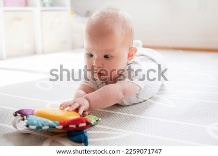 Little baby girl is playing with a toy during tummy time. Baby reaching for a musical toy. Baby development Royalty-Free Stock Photo #2259071747