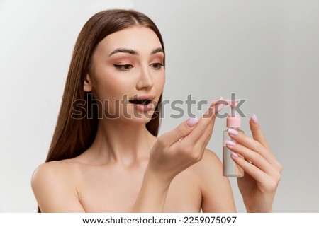 Young beautiful girl with perfect healthy skin applying gel, face cleanser over grey studio background. Concept of natural beauty, skin care, cosmetology, organic cosmetics, health, plastic surgery