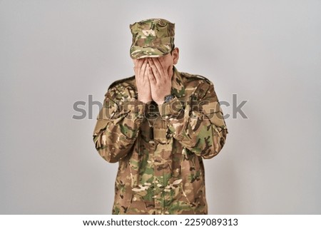 Young arab man wearing camouflage army uniform with sad expression covering face with hands while crying. depression concept. 