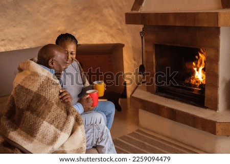 Senior couple sitting around the fireplace with the blanket over them because of the cold weather. Concept: winter, cold, cozy.