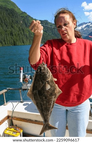 A Fisherwoman Fishing in Alaska holding a Halibut Flatfish she just Caught