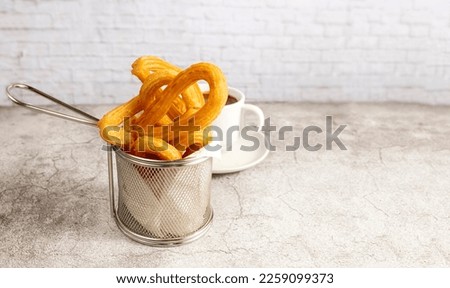 Basket of churros with a cup of chocolate, typical breakfast in Spain on a light background, close up