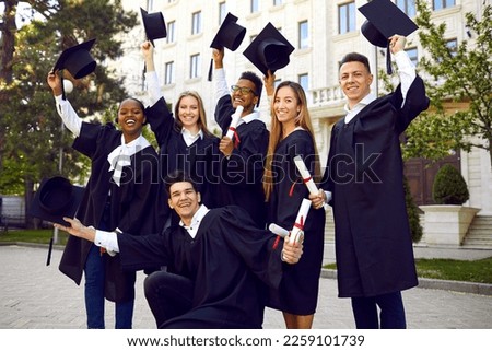 Young multinational people university students dressed in black gown raise their hats rejoicing in successful completion higher education with excellent grades standing in front of college building Royalty-Free Stock Photo #2259101739