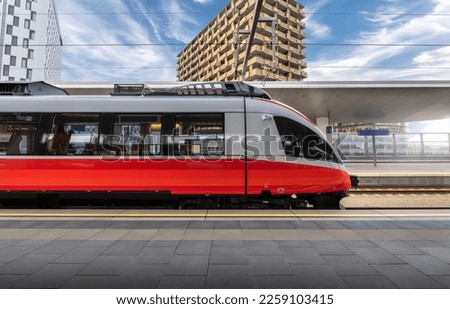 High speed train on the train station at sunset in Vienna, Austria. Beautiful red modern intercity passenger train on the railway platform, buildings. Side view. Railroad. Commercial transportation Royalty-Free Stock Photo #2259103415
