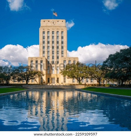 Houston City Hall building skyline, waving American Flags, and live oak trees with water reflections on the Herman Square water fountain in Texas, USA