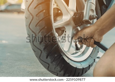 Hands of man check inflator pressure and inflates a tire on motorcycle with an air compressor. Man checking air pressure and filling the tire pressure on the motorbike wheel from automatic air filler. Royalty-Free Stock Photo #2259109877