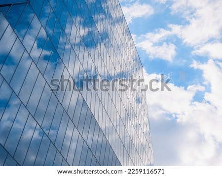 The sky with white clouds reflecting in the glass windows of a modern office building.