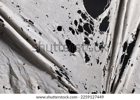 old dirty ragged cloth with holes, grunge damaged cloth on black background, ripped white fabric with many holes Royalty-Free Stock Photo #2259127449